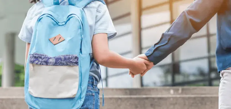 child with backpack walking into school