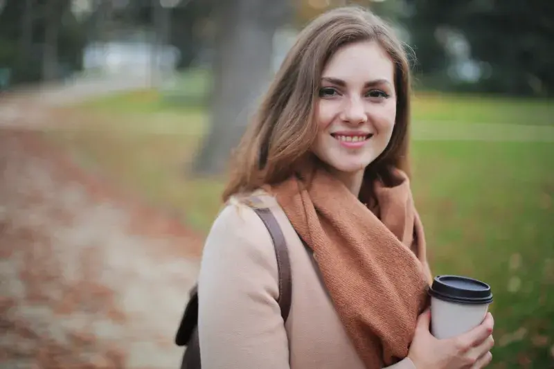 young woman walks in fall weather holding a coffee