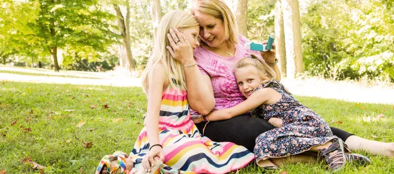 A mother sits on a lawn with her two daughters.